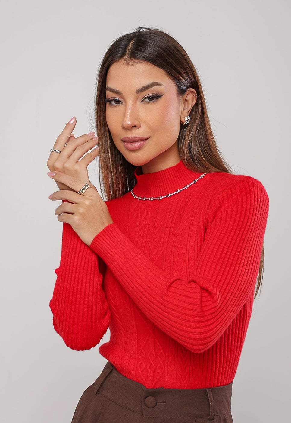 Mulher usando colar riviera dourado e prata com fundo vermelho vivo, braços erguidos